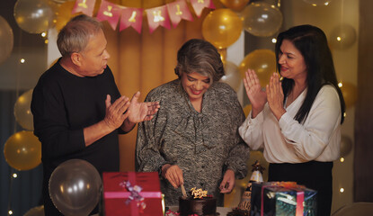 Indian happy adult old elder female male man clap hand sing song aged lady wife hold knife cut cake pastry enjoy party day light decor home older gen x funny group gift have night fun joy spend time