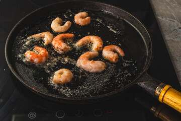 The shrimp are fried in butter in a cast-iron skillet. Cooking large, king prawns. Selected focus.