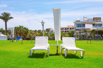 Sunbeds and umbrellas on green lawn in luxury resort. Place for perfect summer vacation 