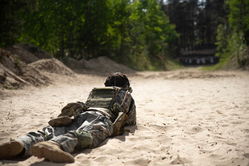 A soldier in camouflage lies on the sand and shoots