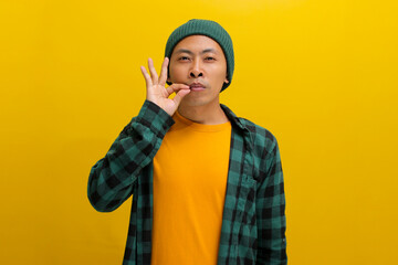 an Asian man, dressed in a casual shirt and wearing a beanie hat, is gesturing for silence by...