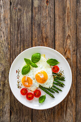 Tasty breakfast. Sunny side up eggs with cooked green asparagus and fried tomatoes served on wooden table
