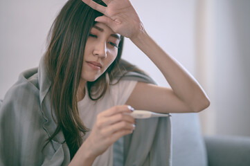 Young Asian woman have a cold and high fever while checking body temperature by using digital...