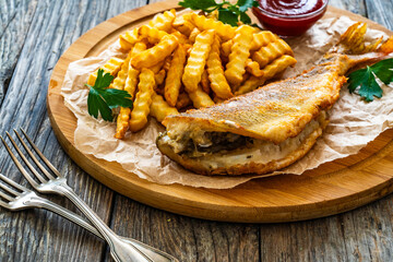 Fried sea bass served on paper with French fries and ketchup on board on wooden table 