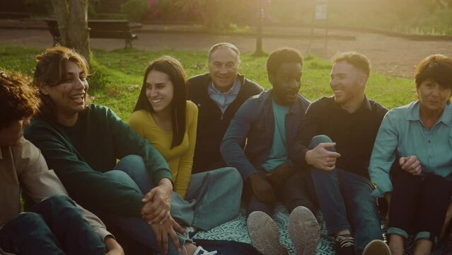 Happy multi generational people having fun sitting on the grass in a public park - Diversity and friendship concept