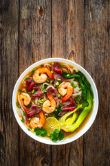 Shrimp and beef Pho soup - Vietnamese soup with shrimps and raw beef slices on wooden table
