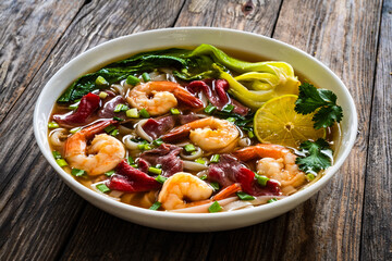 Shrimp and beef Pho soup - Vietnamese soup with shrimps and raw beef slices on wooden table
