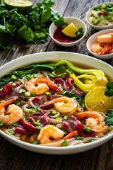 Shrimp and beef Pho soup - Vietnamese soup with shrimps and raw beef slices on wooden table
