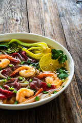 Shrimp and beef Pho soup - Vietnamese soup with shrimps and raw beef slices on wooden table
