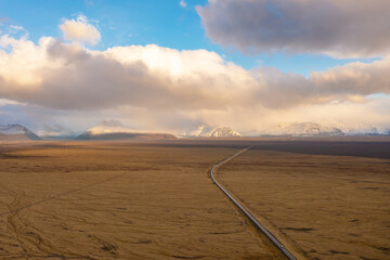 Fototapeta premium Road through valley of volcanic lava, covered with ash and sand. Sunset clouds. East of Iceland.