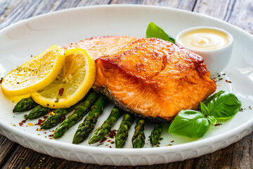 Fried salmon steak with cooked green asparagus and mayonnaise served on wooden table
