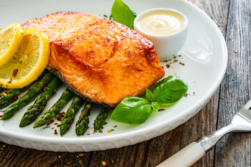 Fried salmon steak with cooked green asparagus and mayonnaise served on wooden table
