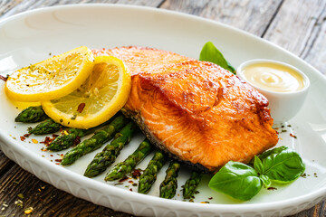 Fried salmon steak with cooked green asparagus and mayonnaise served on wooden table
