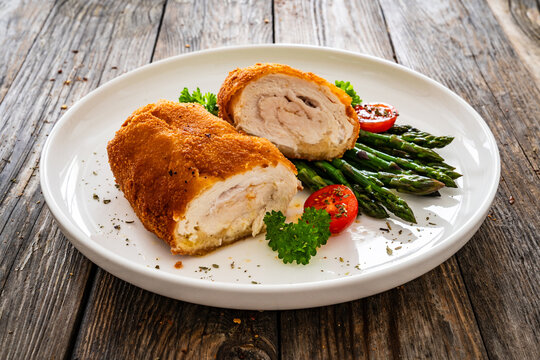 Cutlet de Volaille, wrapped chicken cutlet served with cooked green asparagus on wooden table
