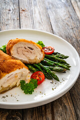 Cutlet de Volaille, wrapped chicken cutlet served with cooked green asparagus on wooden table

