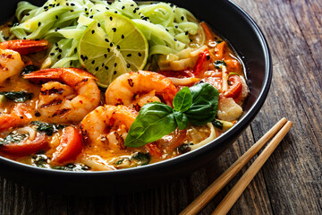 Tom Yam Kung soup - Thai soup with shrimps and rice noodles served in black bowl with chopsticks on...