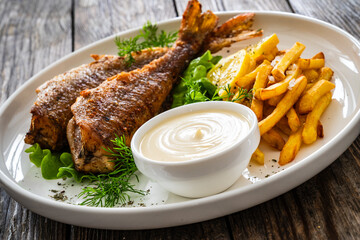 Fried sea bass served on lettuce with French fries, lemon and mayonnaise on white plate on wooden...