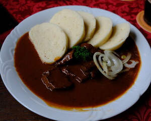 Traditional Czech goulash in black beer sauce served with sliced dumplings and raw onion rings on a...