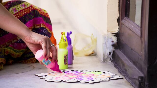 Indian woman in traditional indian clothing using bottles of color powder to make rangoli a traditional art made on floors during festivals of diwali, dussera, onam in hindu culture