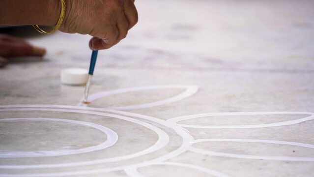 Woman using a paintbrush to make designs on ground for a rangoli a traditional art made on floors during festivals of diwali, dussera, onam in hindu culture