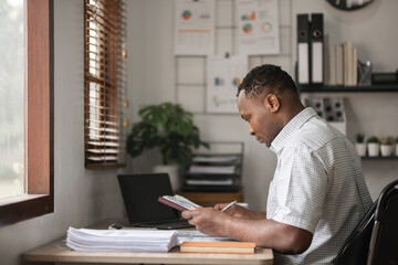 Fototapeta premium African American businessman working on paperwork, searching for information with laptop at home office