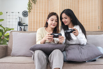 Young LGBT woman, lesbian couple, sitting on the sofa, playing games on a joystick together, having...