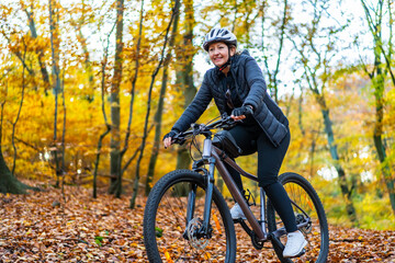 Mid-adult woman riding bicycle in city forest in autumnal scenery

