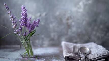 High perspective of a table arrangement with lavender flowers, a napkin, and silver flatware against a blurry gray background