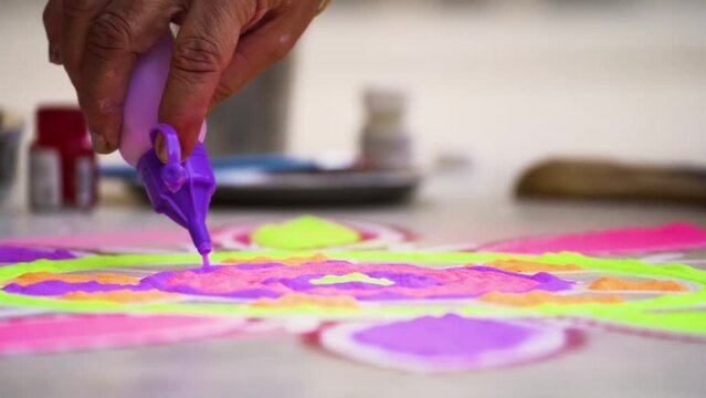 Slow motion shot woman filling purple color from a bottle into a rangoli a traditional art made on floors during festivals of diwali, dussera, onam in hindu culture