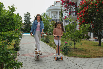Obraz premium Happy mom and daughter walking their rough coated jack russell terrier. Little girl riding a push scooter with her mother and wire haired pup. Copy space, background.