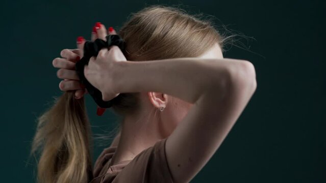 Side view of young woman doing ponytail with scrunchy on dark background