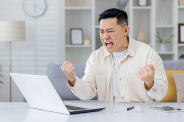 Obraz premium An adult man expressing frustration and anger while working from home, upset with laptop screen. This image captures an intense moment of emotional stress in a remote work environment.