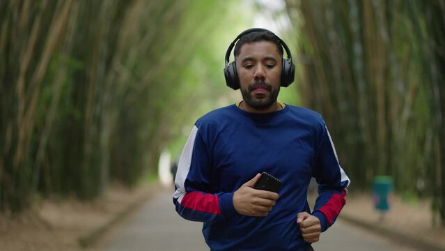 Young sporty queer man runner, morning run in the city urban park Running outdoors healthy active sport lifestyle. fitness gay man jogging. listens to music or a podcast in headphones
