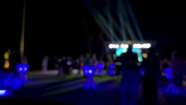 Crowd of people dancing on the dance floor of a night club under the light of colored spotlights and laser. People jump and raise their hands up