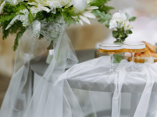 two glasses of sparkling wine on the table covered with tulle. Elegant table setting in pastel white colors for a wedding.