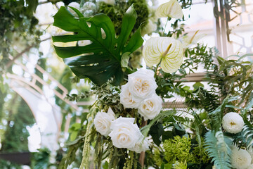 A fragment of a wedding arch decorated with flowers. The flower arrangement consists of different types of roses and green leaves