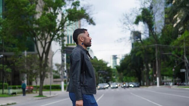 Portrait confident queer fashion man walking in stylish outfit outdoors. Thoughtful man crossing street outdoors at city. Young business gay man at street.

