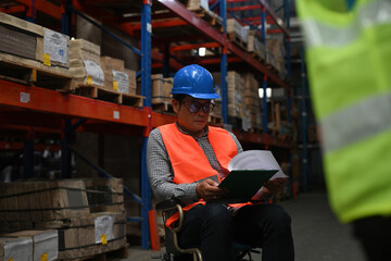 Senior manager with disability in a wheelchair checks stock work at warehouse, the concept of workers with disabilities, accessible workplace for employees with mobility impairment