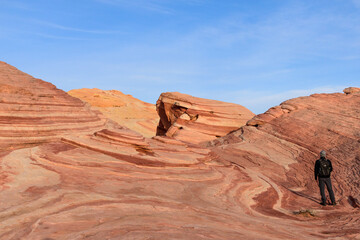 A male hiker takes in the stunning view of the striped rock formation known as the Fire Wave - Valley of Fire State Park, Nevada, USA