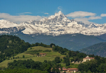 Monviso mountain range completely covered in snow in contrast with the green hills at the bottom of...