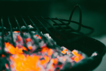 Barbecue coals smolder on the surface of a metal grate. Picnic in nature. Fire flames. Dark...