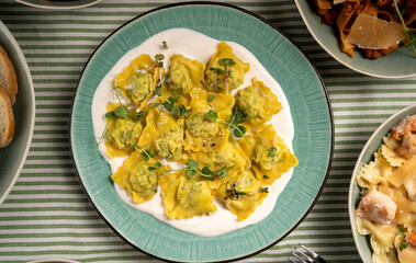 Italian ravioli with spinach and cheese on blue plate serving at table with other dishes. Italian cuisine concept