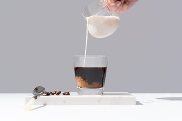 Verter leche en un vaso transparente de café sobre mármol y fondo gris	