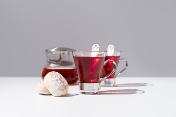 Dos tazas de té rojo con pasteles y dulces sobre mesa blanca y fondo gris	