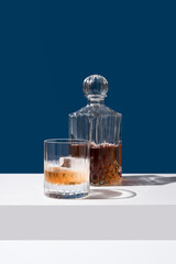 Un vaso de whisky escocés con hielo y decantador sobre fondo azul	