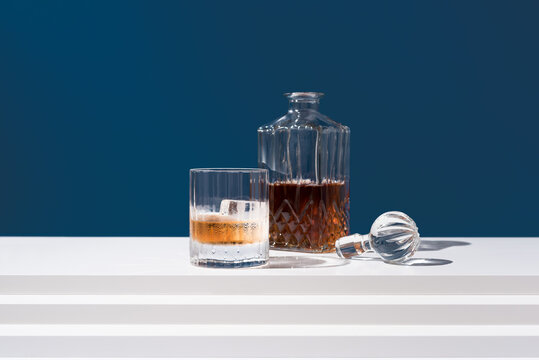 Un vaso de whisky escoc&eacute;s con hielo y decantador sobre fondo azul	