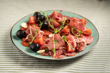 Food plate with delicious salami, sliced ham, sausage, tomatoes and black olives. Meat platter with cured meat on a celebratory table.