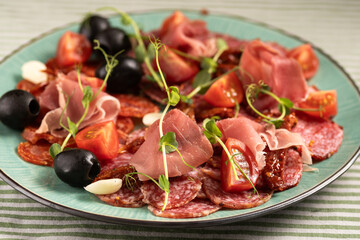 Food plate with delicious salami, sliced ham, sausage, tomatoes and black olives. Meat platter with cured meat on a celebratory table.