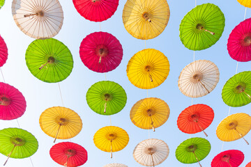 Colorful paper umbrellas float in the sky tied with strings against the background of the sky.