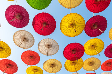 Colorful paper umbrellas float in the sky tied with strings against the background of the sky.